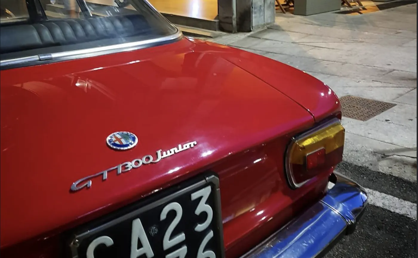 Il posteriore di una Alfa Romeo GT 1300 Junior rossa parcheggiata di sera davanti al portico.