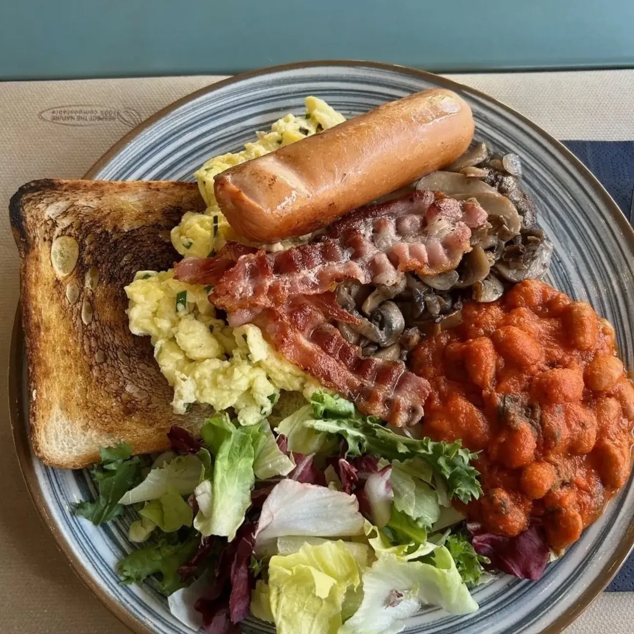 Piatto di colazione all'inglese con uova strapazzate, bacon, salsiccia, funghi, fagioli, insalata e pane tostato.