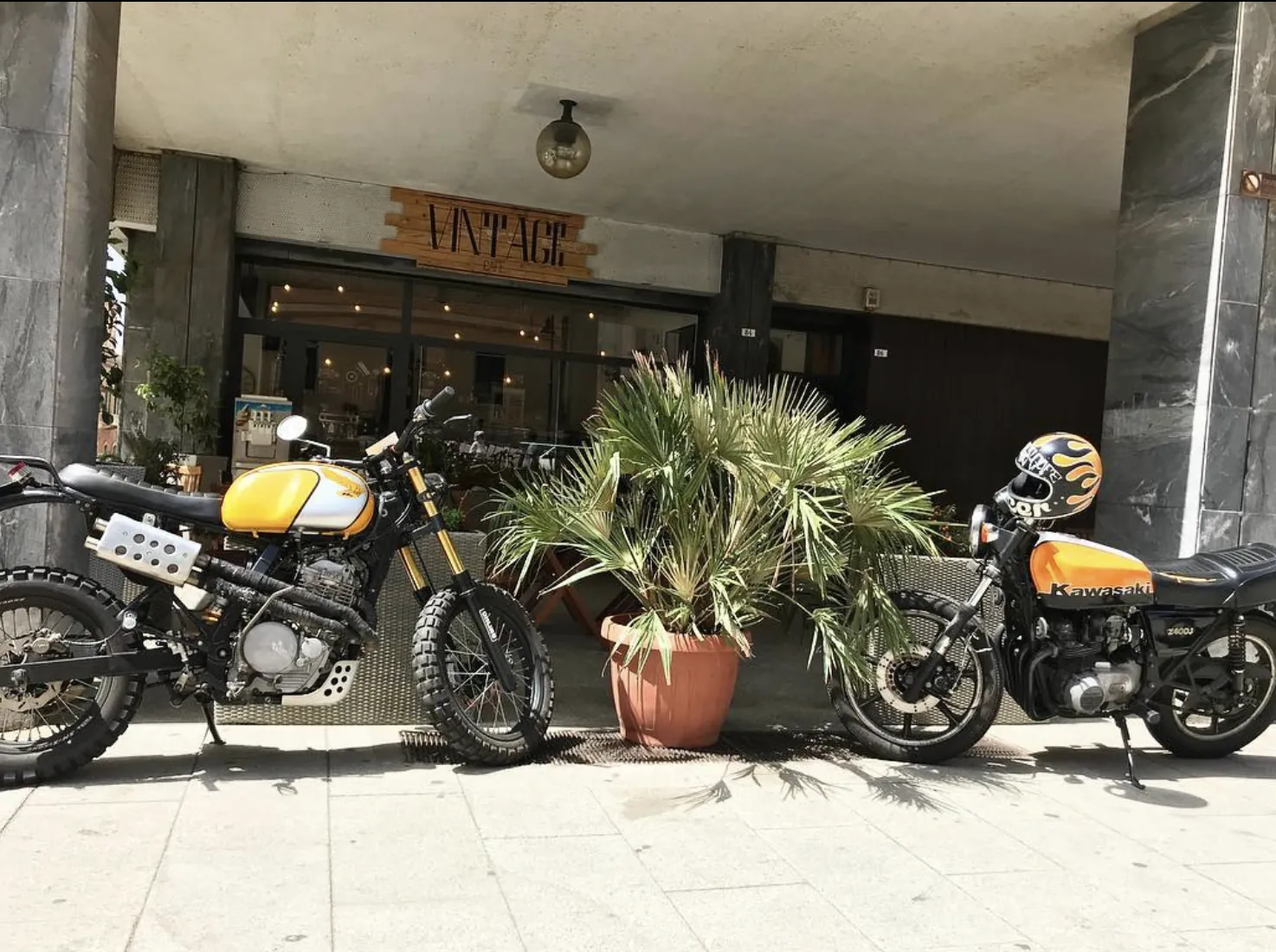 Due moto d'epoca parcheggiate davanti all'ingresso del Vintage Cafè, con l'insegna di legno sopra la vetrina.