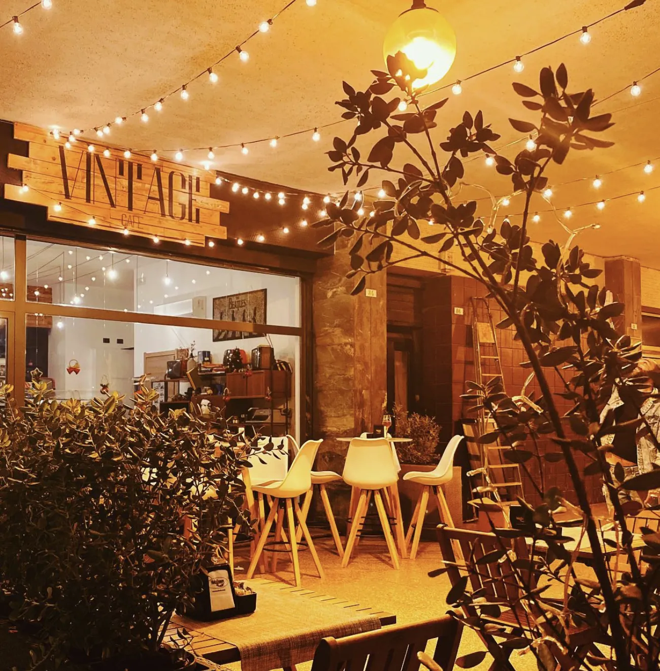 I tavolini del Vintage Cafè sotto il portico di via Mameli, la sera, con l'insegna di legno e le lampadine appese.