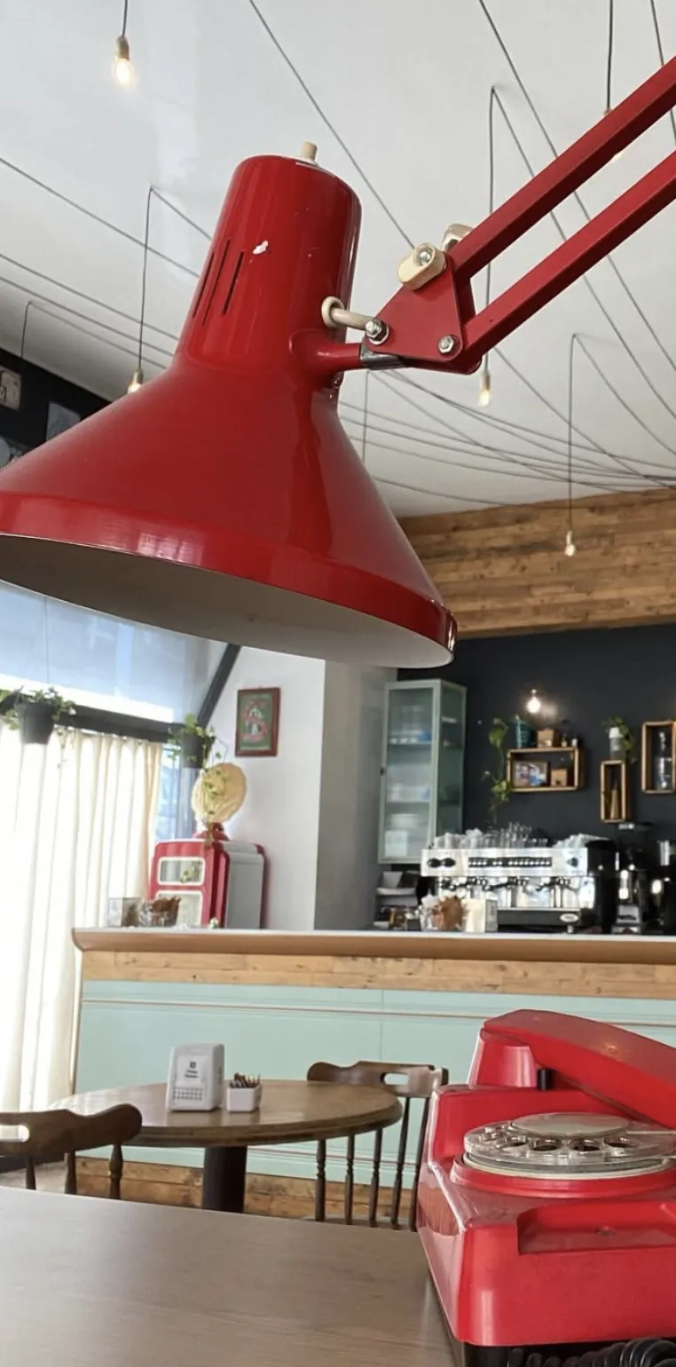 Interno del bar: la lampada snodata rossa appesa al soffitto, il telefono a disco rosso sul tavolo e il bancone con le ante color menta.